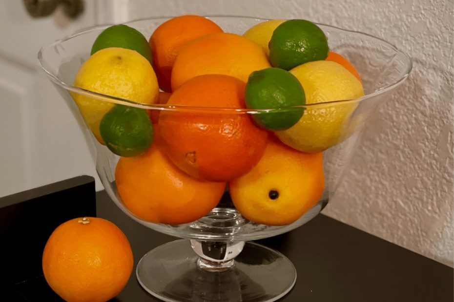 A glass fruit bowl holds oranges, lemons, and limes.