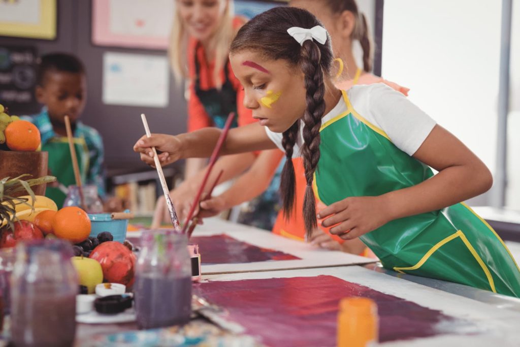 A child painting a colorful picture in a full classroom.