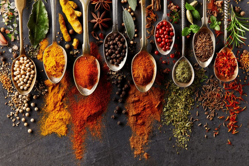 A row of spoons overflowing with varieties of colorful spices.