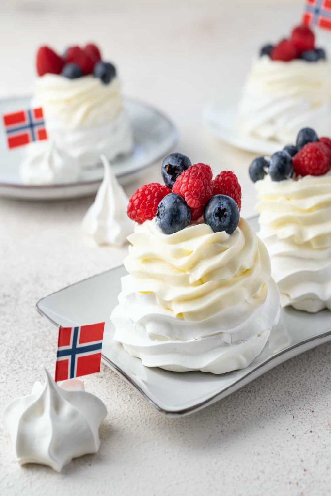 Plates of fluffy merengue desserts decorated with berries and little Norwegian flags.