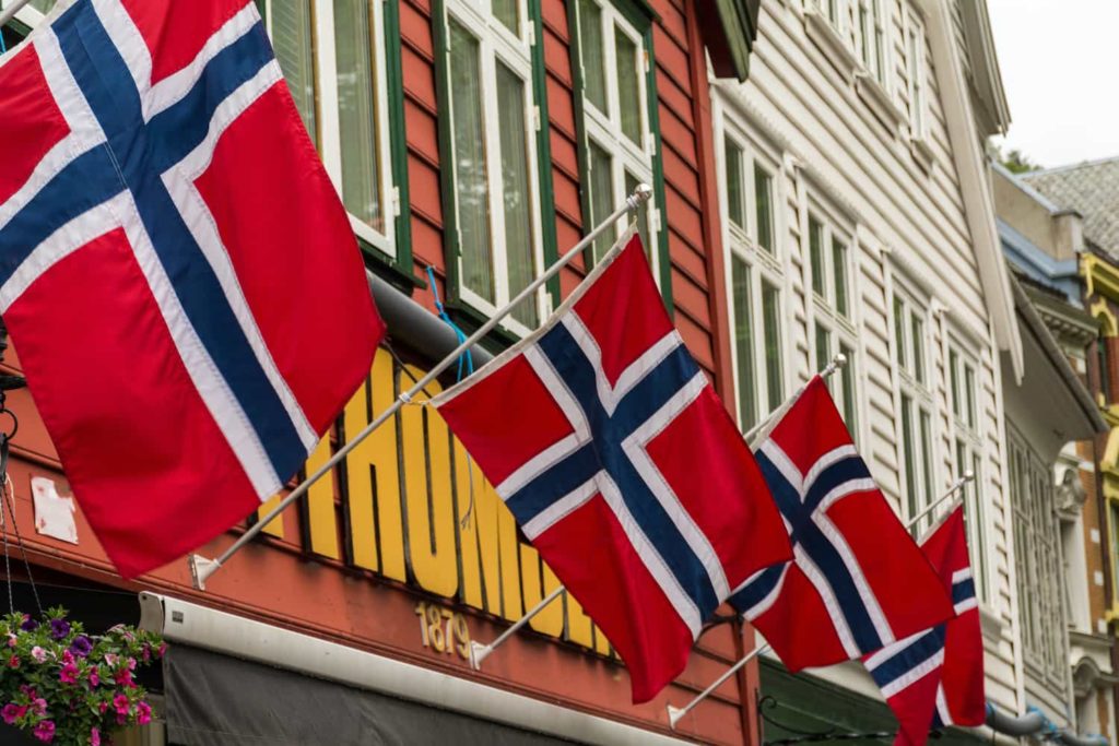 A row of Norwegian flags displayed outside a colorful storefront.