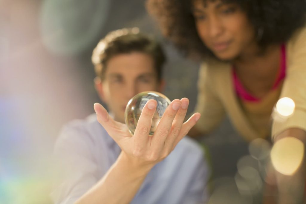 A man and a woman stare at a glass sphere held in the man’s open hand.