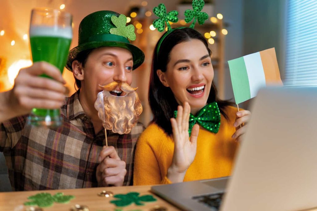 A man and woman holding St. Patrick’s Day props and videoconferencing through a laptop.
