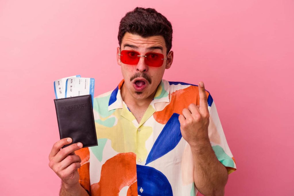 A man in a colorful outfit holding a passport and airplane tickets. He points upwards.