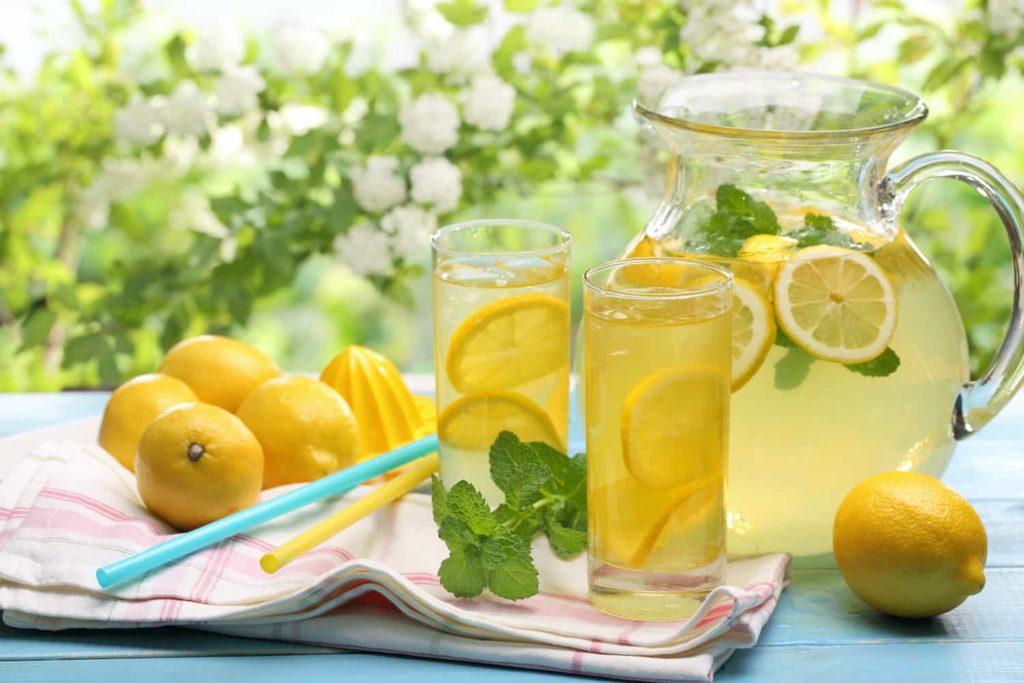 A pitcher of lemonade with two glasses, straws, and an assortment of lemons.