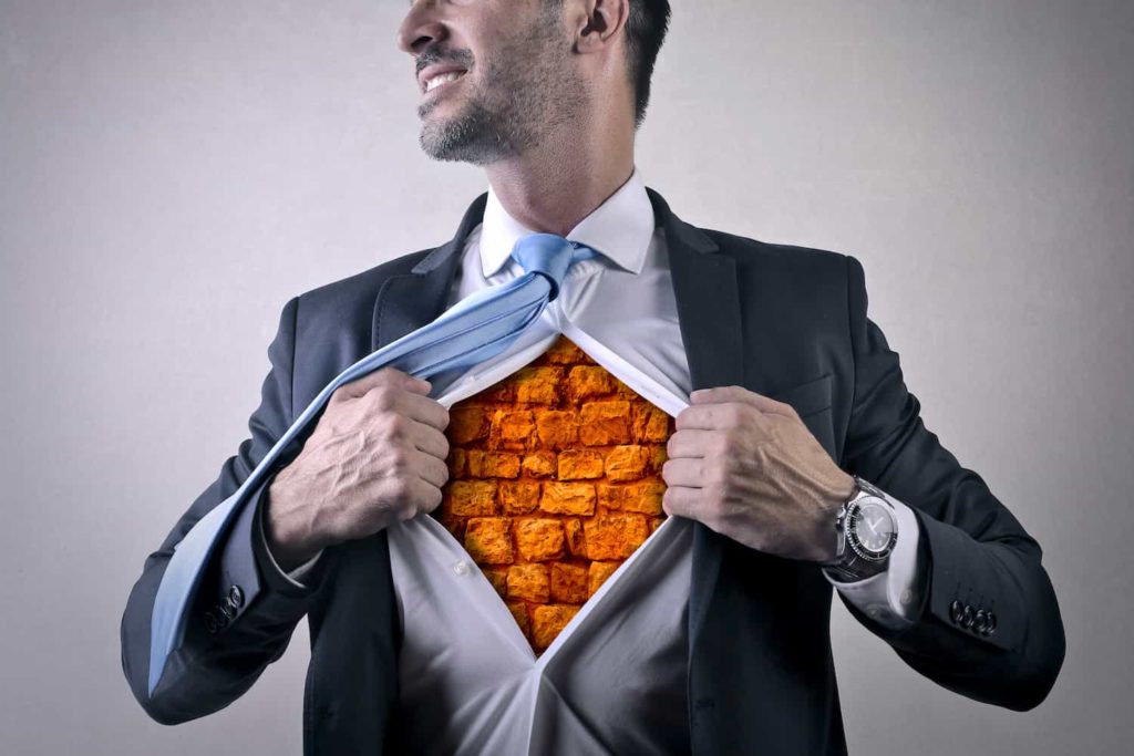 A businessman opens his shirt to reveal a brick wall where his chest should be.