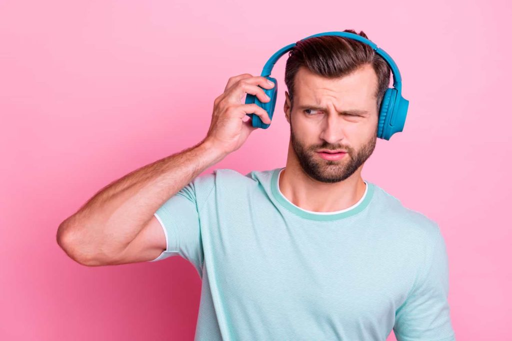 A man wearing headphones pulling one of the earphones away from his ear with a look of disgust.