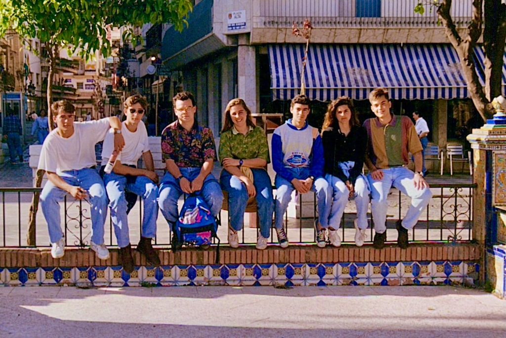 A group of students in 1990s attire sitting on a wall in the south of Spain.