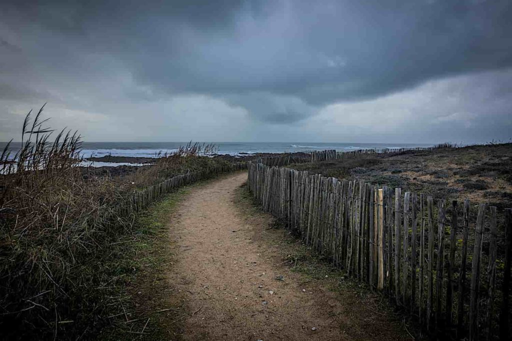 A stark sea-side landscape with dark clouds over a dirt path.