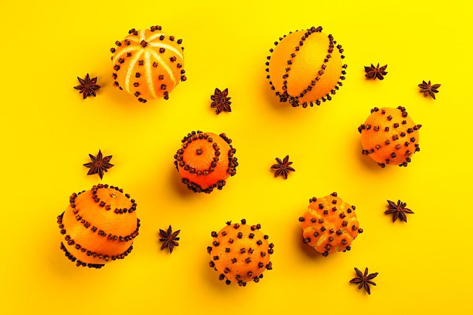 Pomander balls made from oranges and spices displayed on a yellow backdrop.