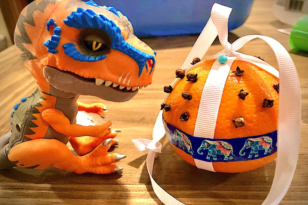 A pomander ball next to a toy dinosaur.