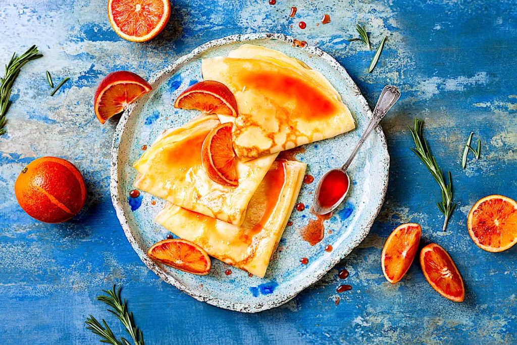 A plate of crepes with oranges and orange marmalade.