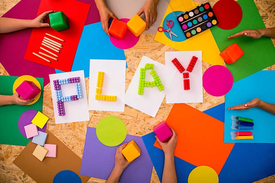 The word “Play” spelled out in colorful blocks on a background of crafting supplies.