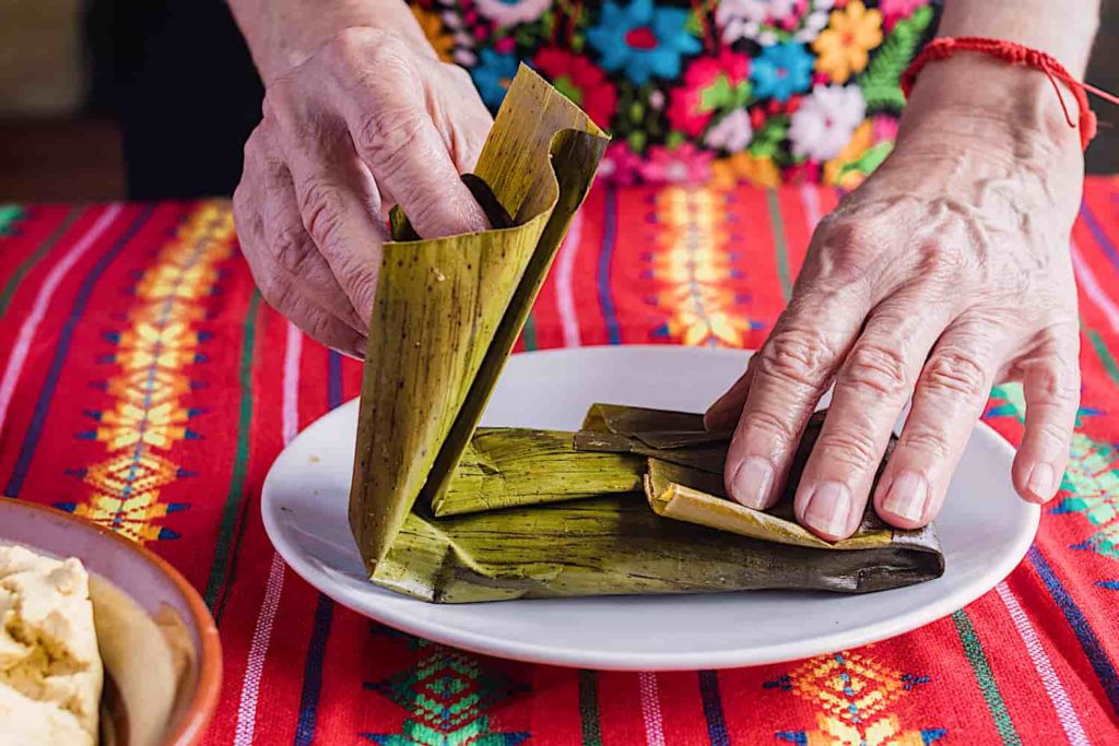 A pair of elderly hands rolling a fresh tamale in a banana leaf.