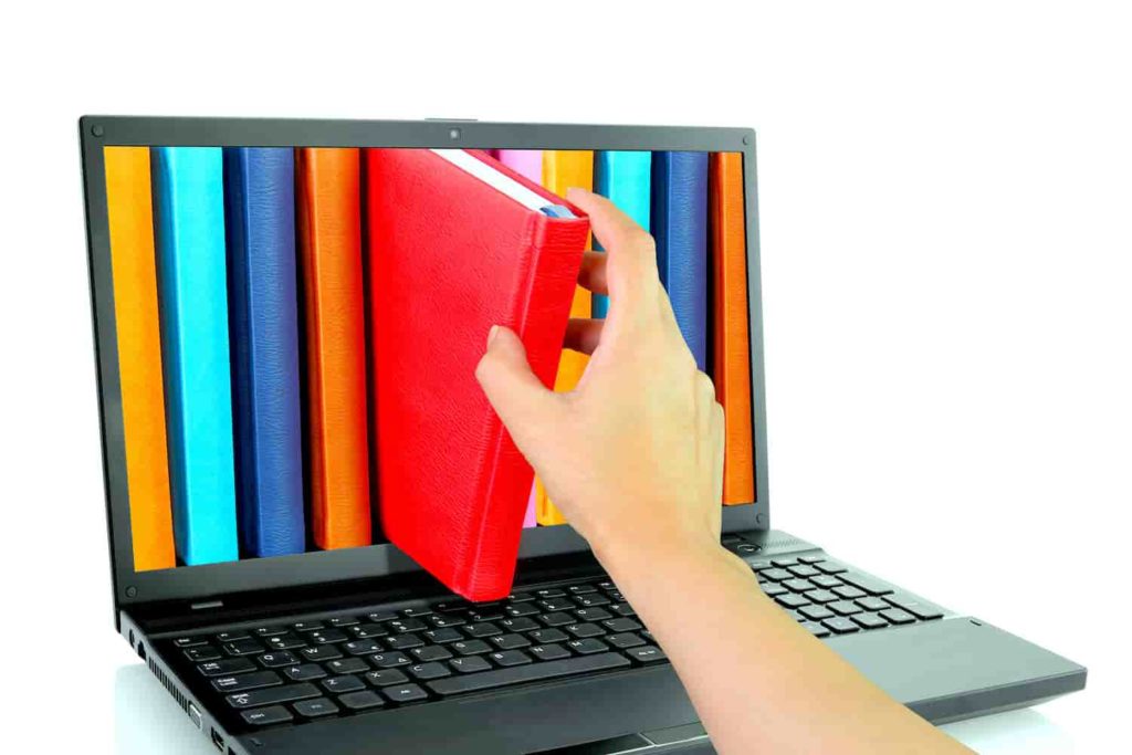 : A picture of a hand pulling a book out of the screen of a laptop computer.