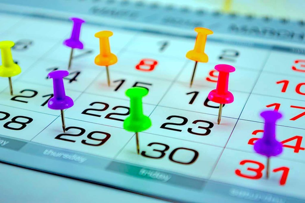 A calendar stuck with multi-colored stickpins.
