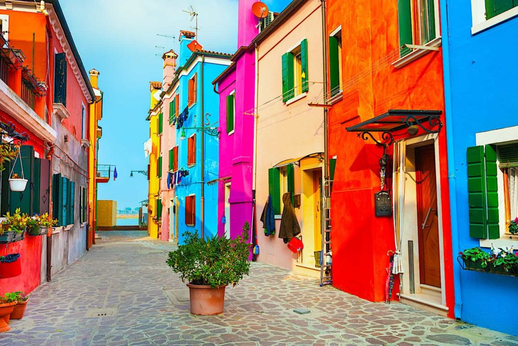 A Venetian street lined with colorful homes leading to the sea.