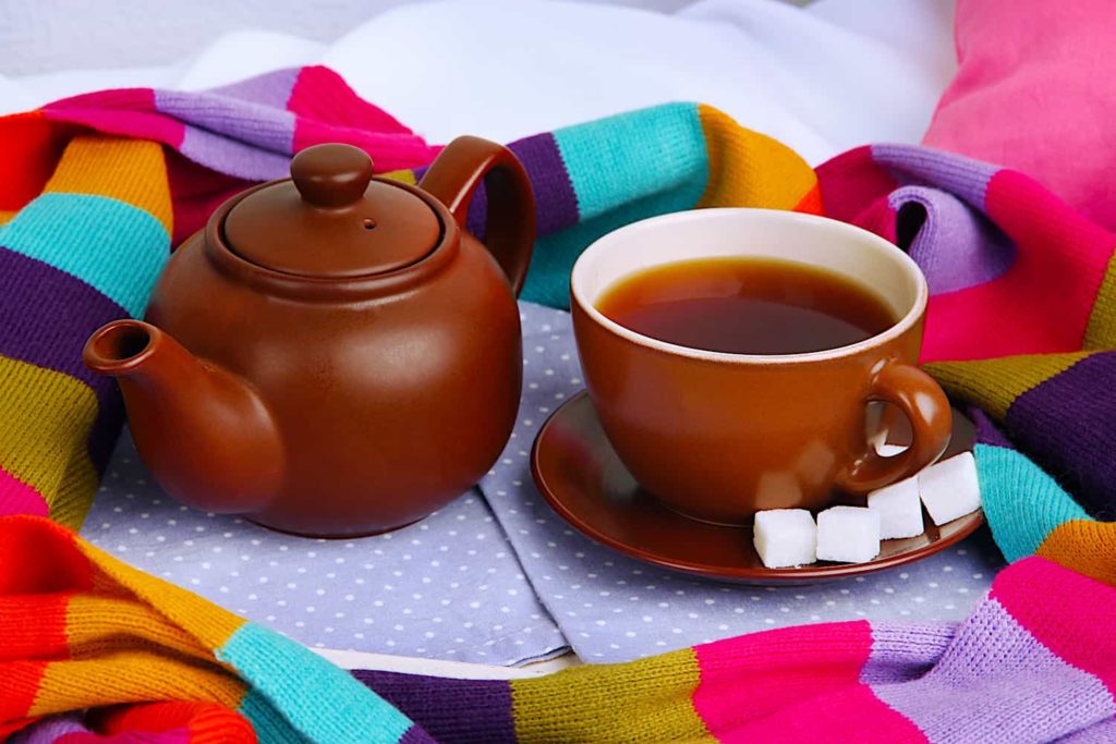 A picture of a ceramic tea pot and cup surrounded by colorful scarf.