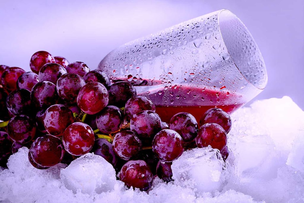 A picture of grapes and a glass of juice tucked into a pile of snow.
