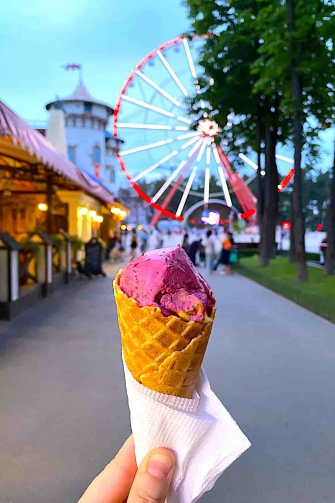 A hand-held waffle cone with pink ice cream; a Ferris wheel in the background.